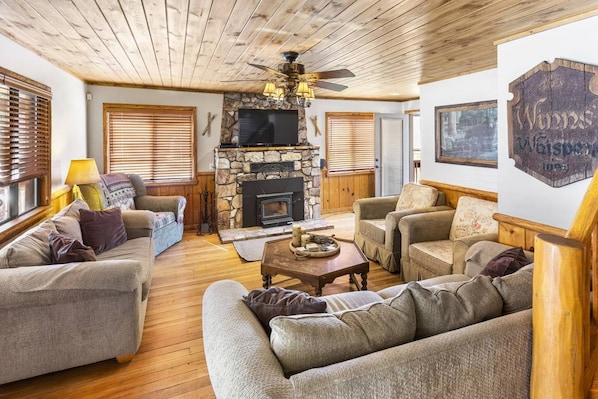A cozy living room with a stone fireplace, wooden ceiling, and comfortable seating.