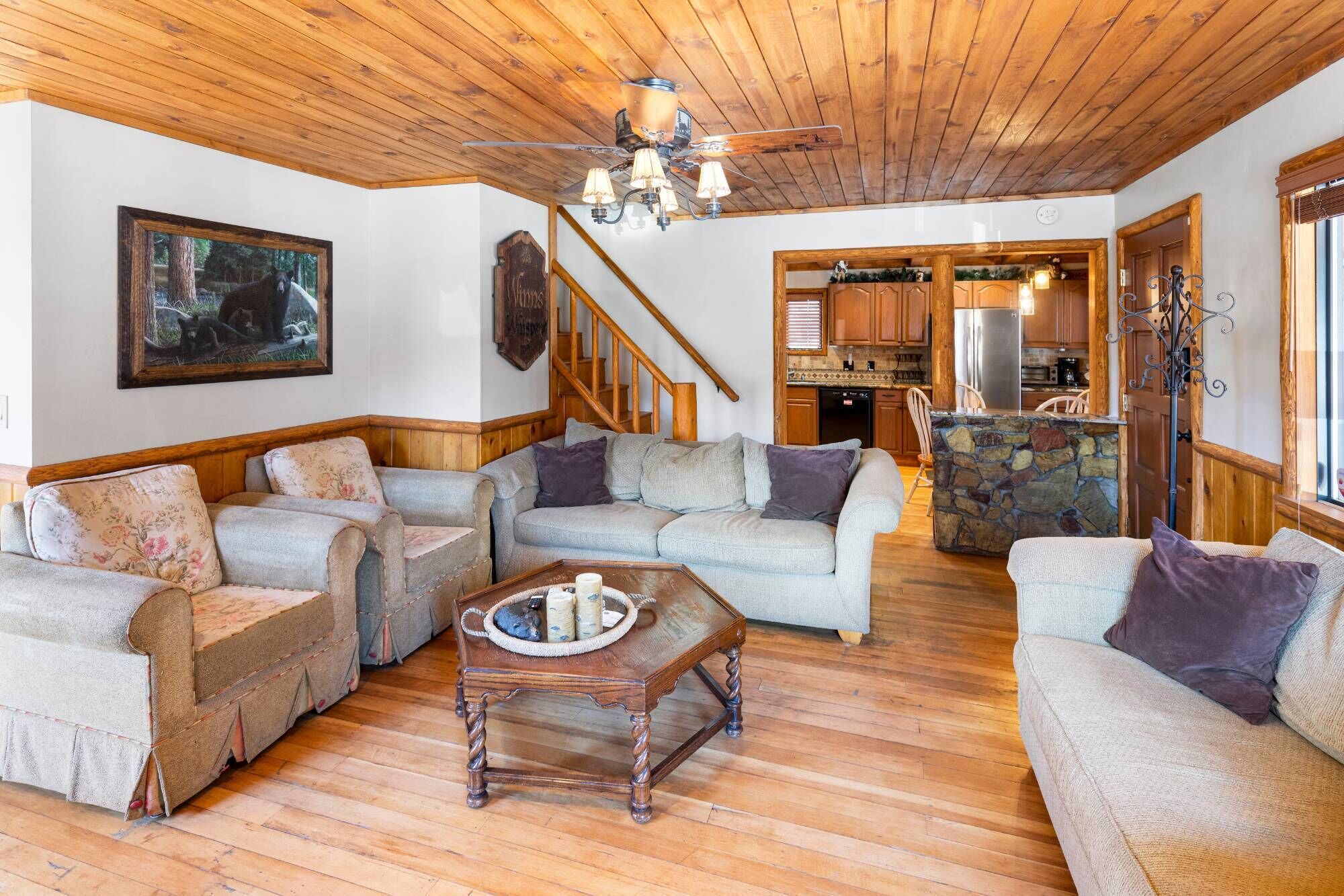 A cozy living room with wooden flooring, a stone fireplace, and a dining area with a kitchen in the background.