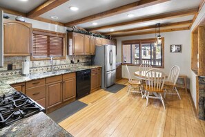 A kitchen with wooden cabinets, a granite countertop, a stainless steel refrigerator, and a dining area with a wooden table and chairs.