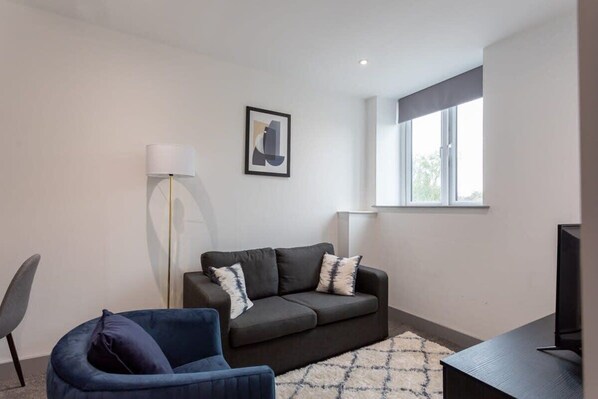 A modern living room with a grey sofa, a blue armchair, a floor lamp, and a TV stand.