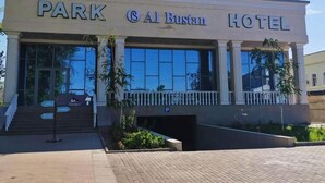 A building labeled "Park Al Bustan Hotel" with a large entrance, steps leading up to it, and a parking sign. - Park Hotel al Bustan (Shymkent)