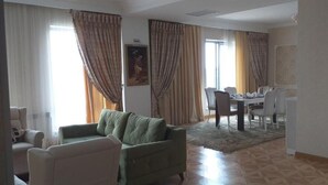 A living room with a sofa, chairs, a dining table with chairs, and a large window with curtains. - Park Hotel al Bustan (Shymkent)