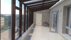 A covered corridor with large windows, a door, and a view of buildings outside. - Park Hotel al Bustan (Shymkent)