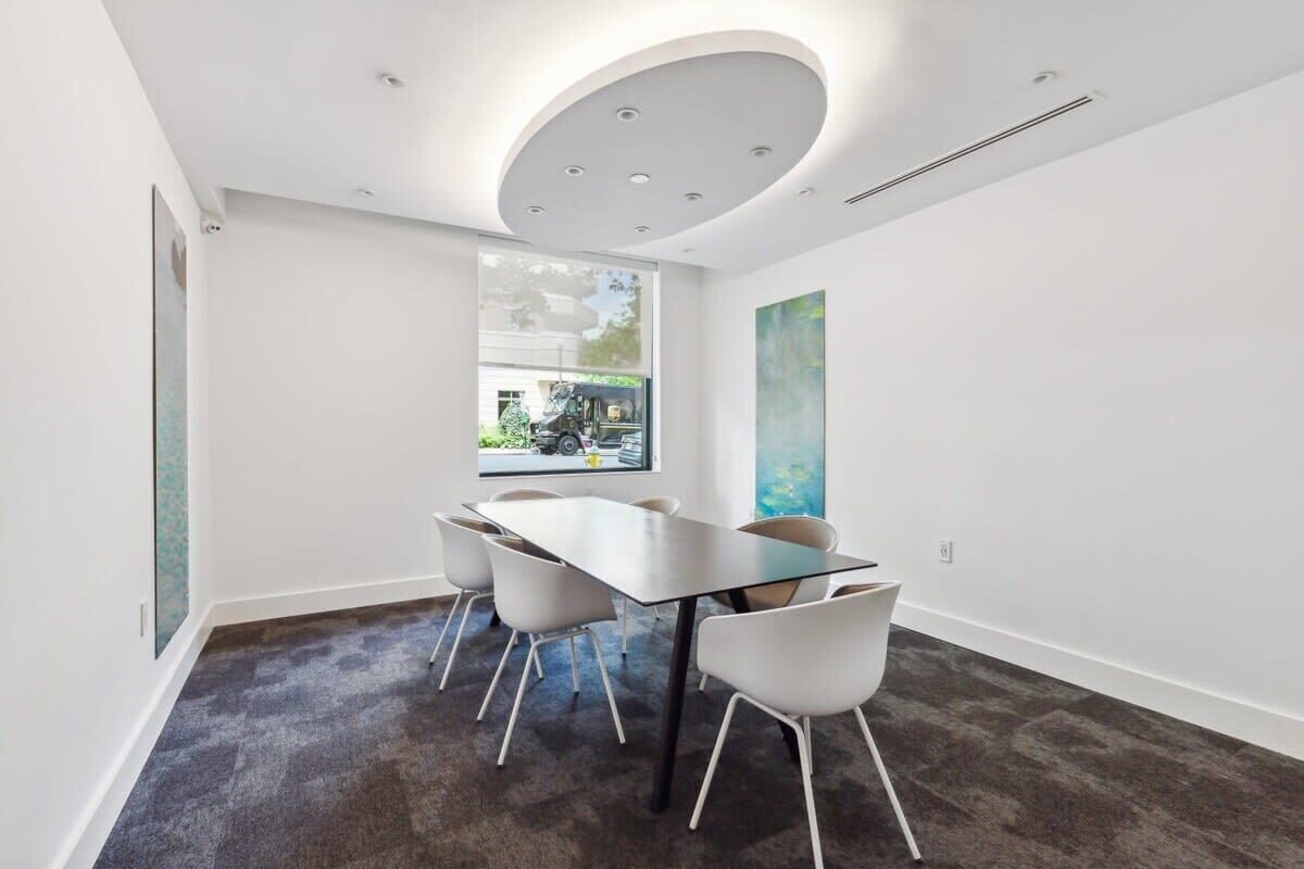 A modern conference room with a glass table, white chairs, and a large window with a view of a vehicle.