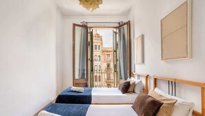 Ein Zimmer mit zwei Betten, Blick auf ein Gebäude durch eine offene Tür und einem gerahmten Bild an der Wand.