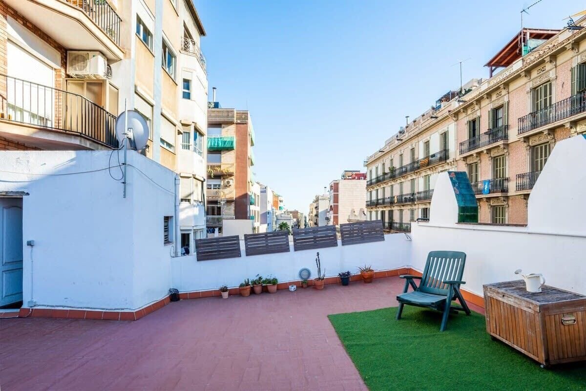 A rooftop terrace with a green lawn, a wooden table, and a chair.