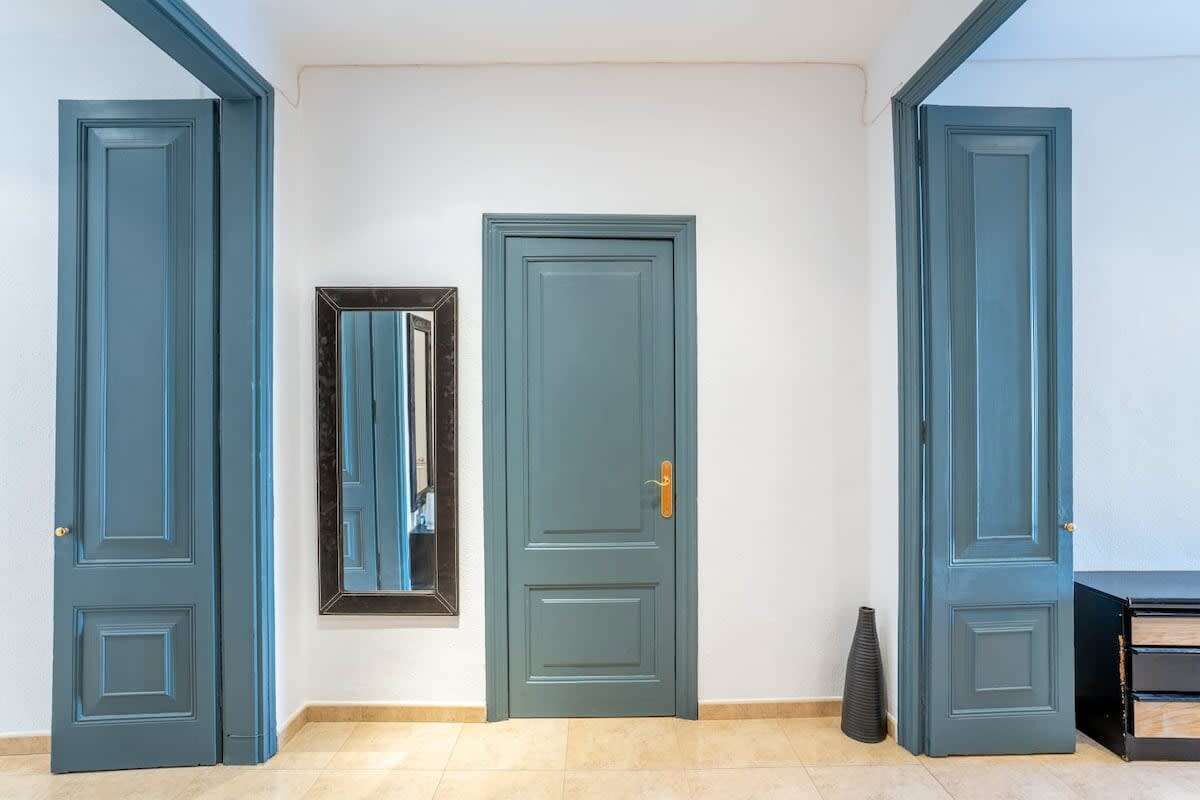 A hallway with three doors, a mirror, and a vase on the floor.