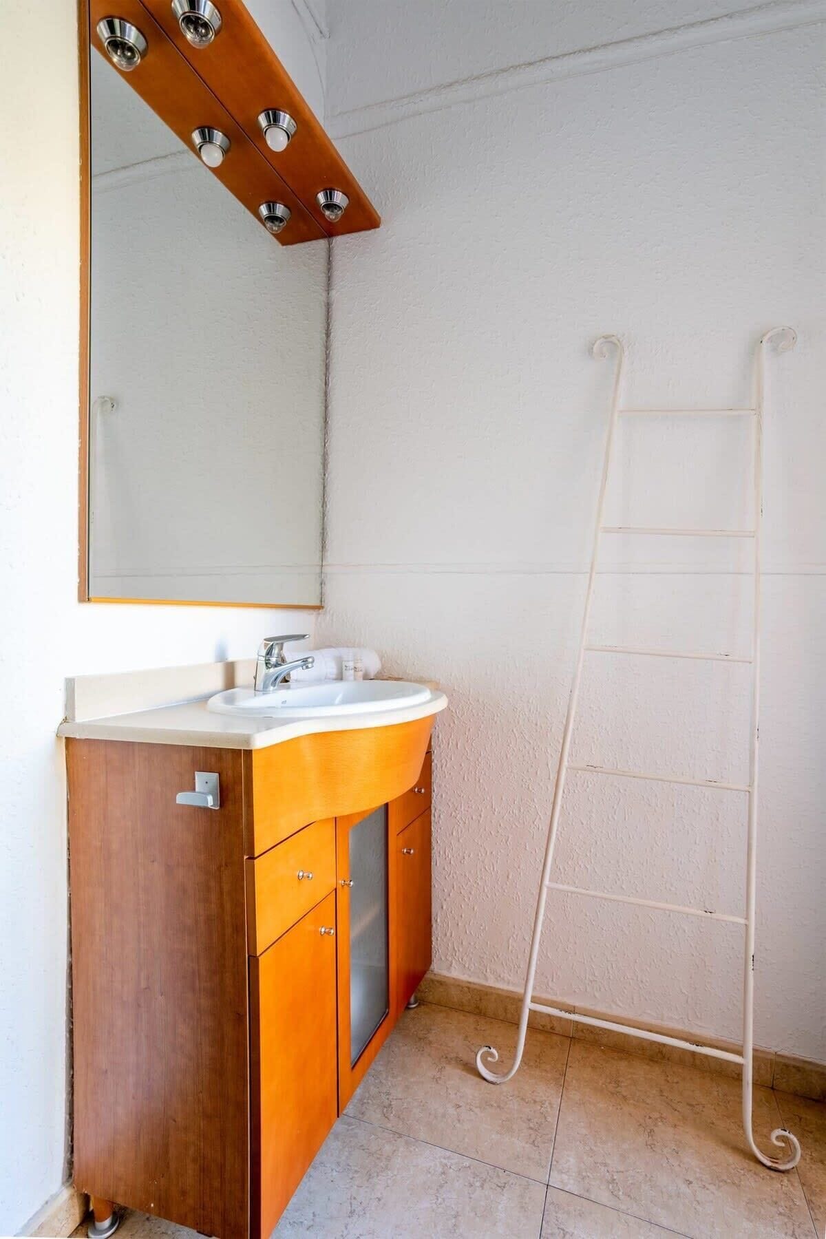 Ein Badezimmer mit einem Holzbadschränken, einem weißen Waschbecken und einer weißen Duschleiter.