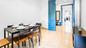 A dining area with a table set for four, a blue door leading to another room, and a hallway with a view into another space. - Private terrace Attico 3BD in Gran de Gracia (Barcelona)