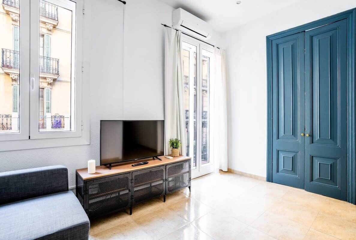 Una sala de estar moderna con un televisor de pantalla plana sobre una consola de madera, ventanas grandes y una puerta azul.