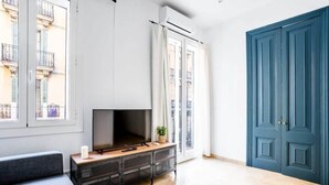 A modern living room with a flat-screen TV on a wooden console, large windows, and a blue door. - Private terrace Attico 3BD in Gran de Gracia (Barcelona)