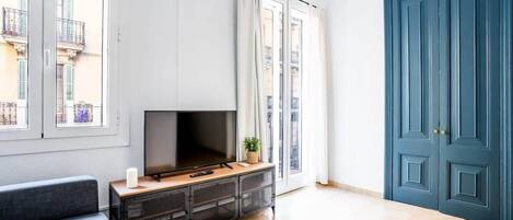 Una sala de estar moderna con un televisor de pantalla plana sobre una consola de madera, ventanas grandes y una puerta azul.