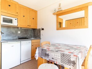 A compact kitchen with wooden cabinets, a microwave, a dishwasher, and a table with a patterned tablecloth.