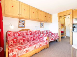 A cozy room with a wooden sofa set, a kitchen area, and a door leading to another room.