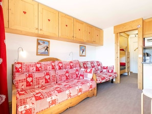 A cozy room with a wooden sofa set, a kitchen area, and a door leading to another room.