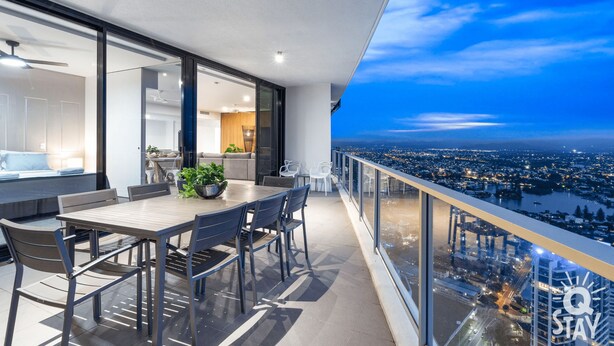 Ein moderner Balkon mit Essbereich, großen Fenstern und Blick auf die Stadt im Abendlicht.