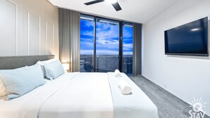 Ein modernes Hotelzimmer mit einem großen Bett, einem Flachbildfernseher und Blick auf die Stadt durch große Fenster.