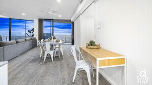 Ein moderner Essbereich mit hohem Tisch und Stühlen, einem Holznachttisch und Blick auf die Stadt durch große Fenster.