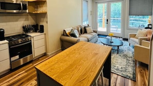 A modern kitchen with a wooden bar counter, a built-in oven, and a microwave. There is a seating area with a sofa and a coffee table.