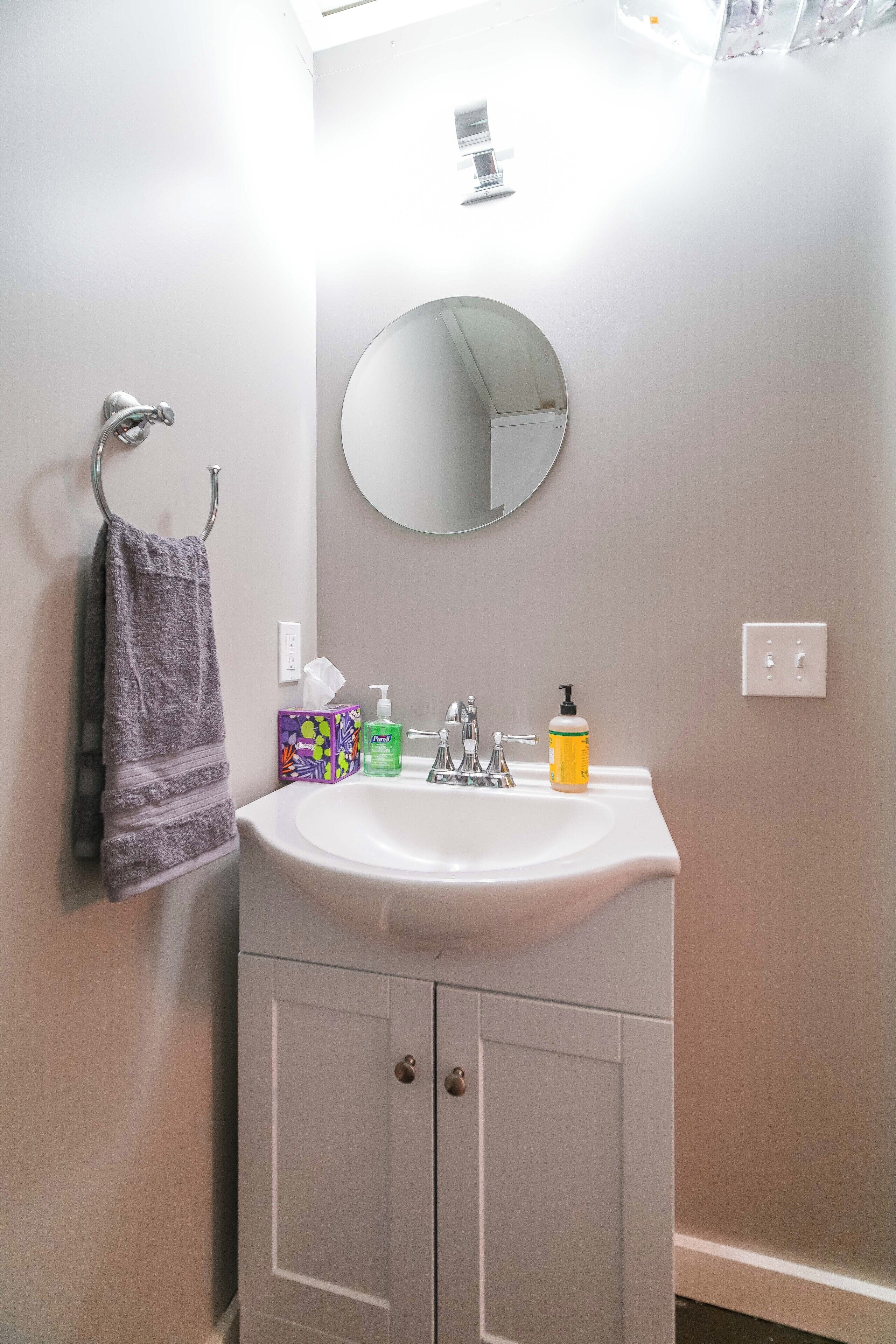 A bathroom with a white sink, a round mirror, and a towel rack.