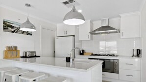 A modern kitchen with white cabinetry, a central island with stools, stainless steel appliances, and pendant lighting.