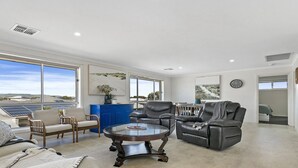 A spacious living room with a large window, a blue cabinet, and a glass coffee table.