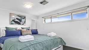 A bedroom with a bed, pillows, a blanket, a painting, and a window.