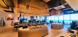 Een modern restaurant met uitzicht op zee, met een buffet vol diverse gerechten, sfeerverlichting en een eigentijds interieur.