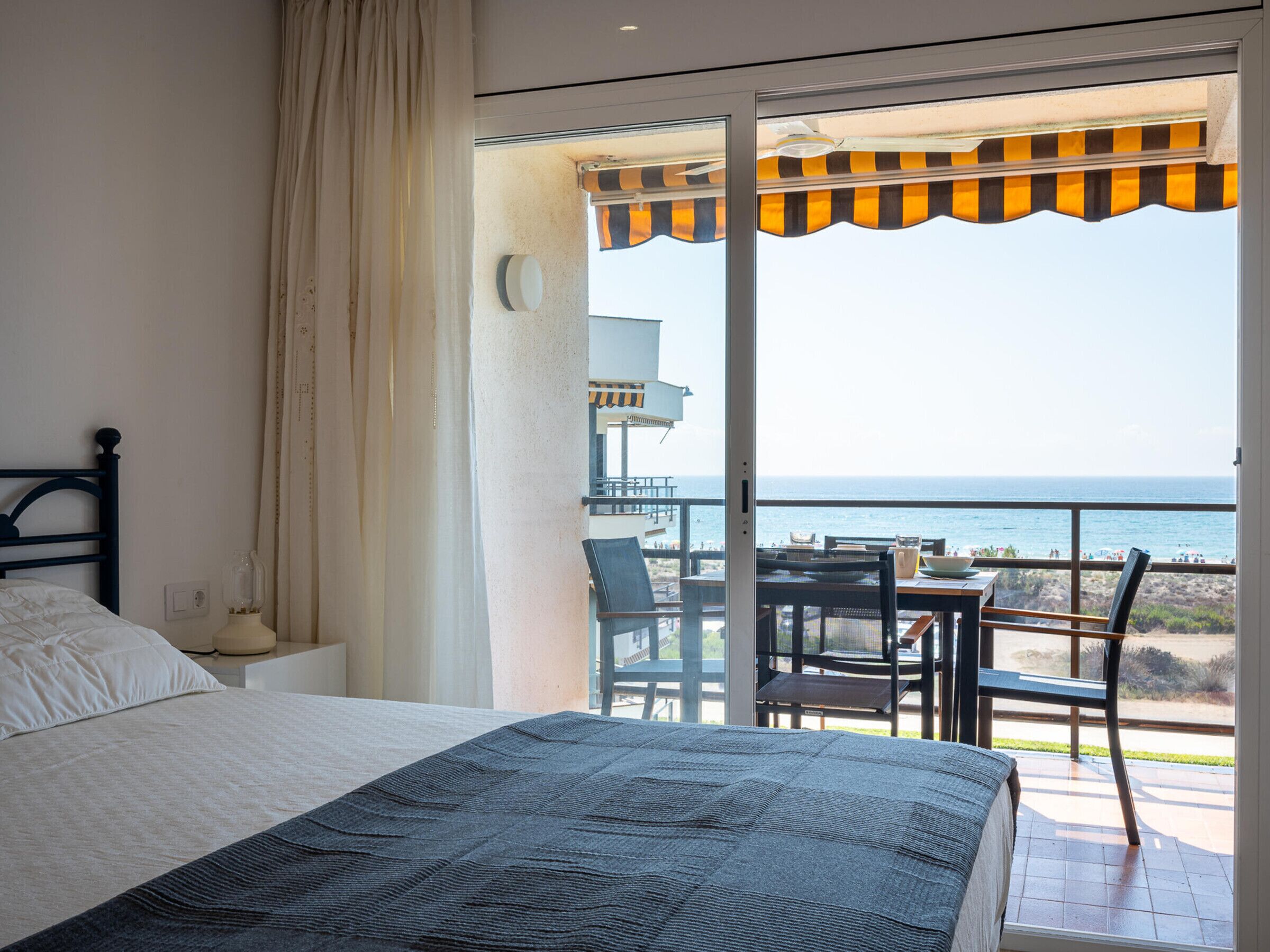 A bedroom with a bed, a nightstand, a lamp, and a view of the ocean through a sliding glass door.