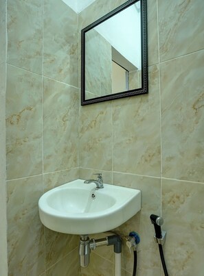 Une salle de bain avec un lavabo blanc, un miroir à cadre noir et des carreaux de marbre aux murs.