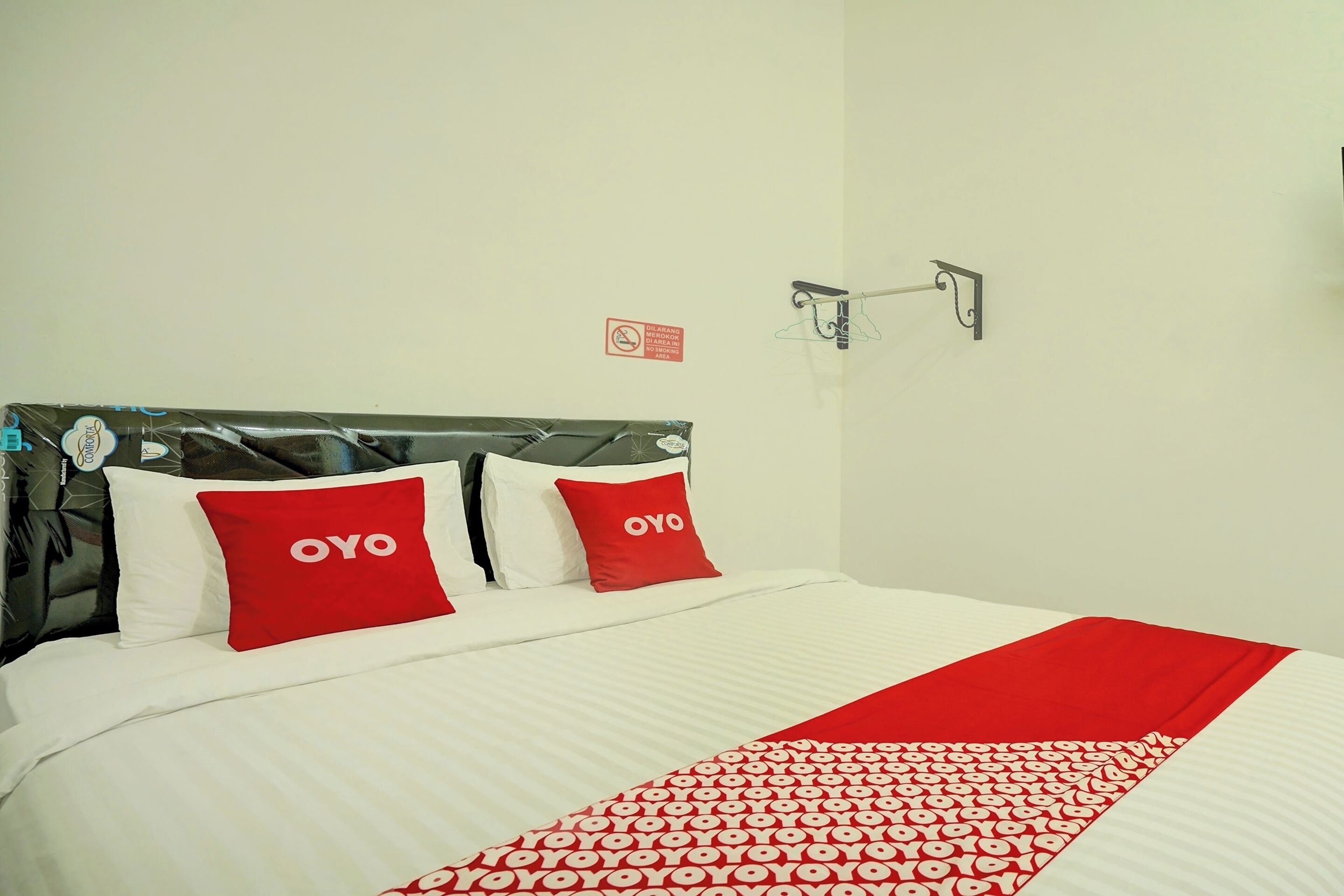 A neatly made bed with white and red bedding, a patterned throw, and a wall-mounted light fixture.