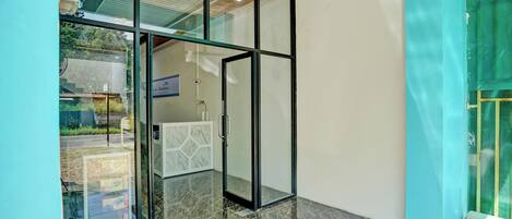 A modern hotel lobby with a glass door entrance, a red mat on the floor, and a view of the outside.