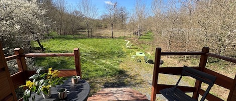 Una terraza de madera con mesa y sillas, con vistas a un área verde con árboles.
