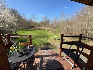A wooden deck with a table and chairs, a bench, and a view of a grassy field with trees. - Cozy Gypsy Caravan Retreat in Berry with Solar Power and Full Amenities (Ardentes)