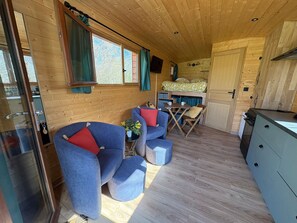 A cozy cabin interior with a dining area, seating with cushions, and a kitchenette. - Cozy Gypsy Caravan Retreat in Berry with Solar Power and Full Amenities (Ardentes)