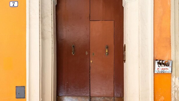 A double door with a white archway, a metal handle, and a small sign on the wall. - Casa sul Canale di Via Piella by Wonderful Italy (Bologna)