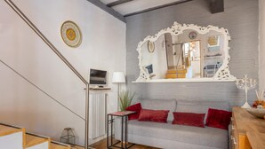 A modern living room with a grey sofa, red cushions, a white ornate mirror, a small table with a lamp, and a staircase with wooden steps. - Casa sul Canale di Via Piella by Wonderful Italy (Bologna)