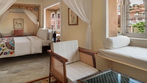 A room with two beds, a chair, a table, and a window with a view of the outside.