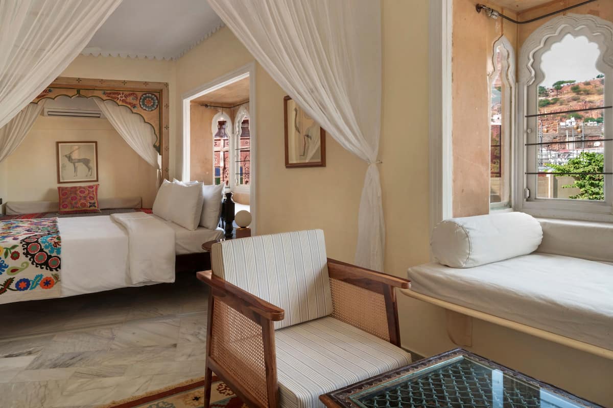 A room with two beds, a chair, a table, and a window with a view of the outside.