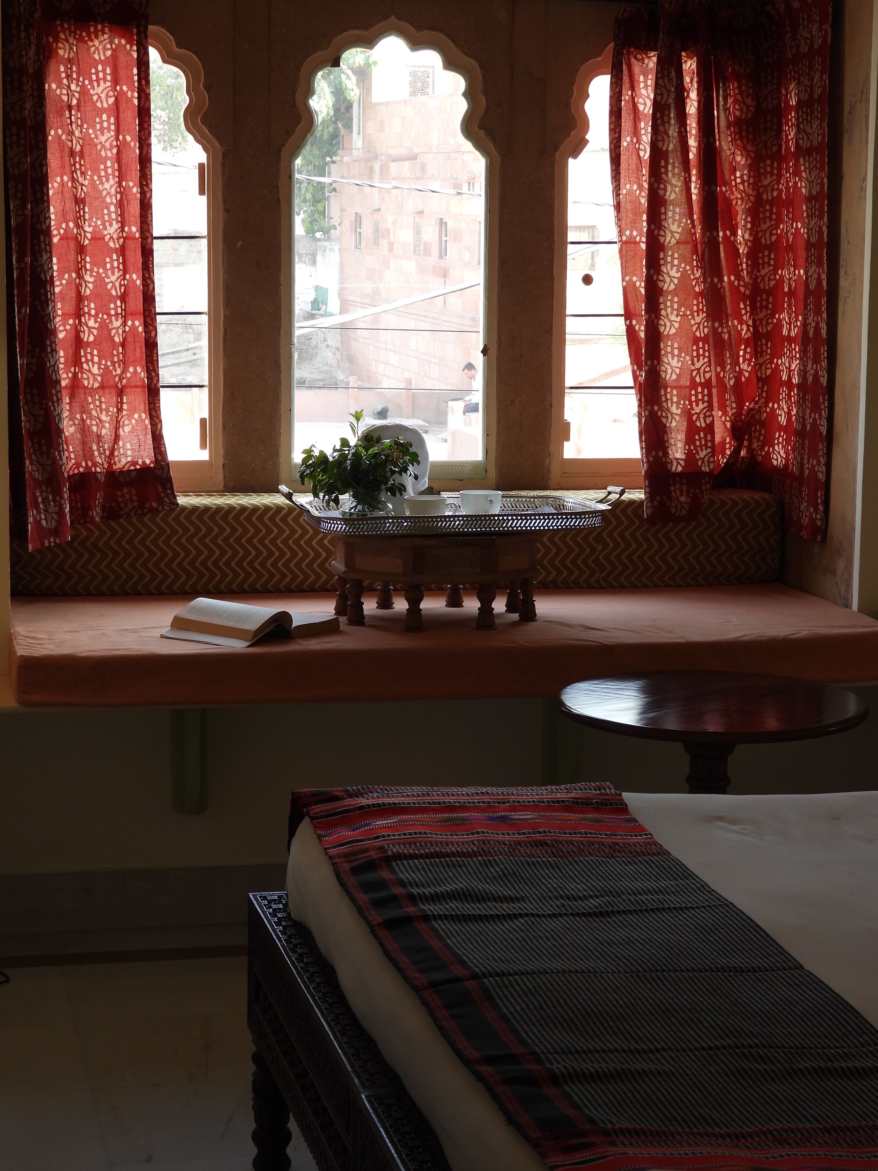 A room with a window seat, a small table with a plant, and a bed.