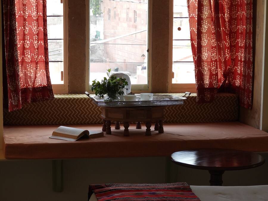 A room with a window seat, a small table with a plant, and a bed.