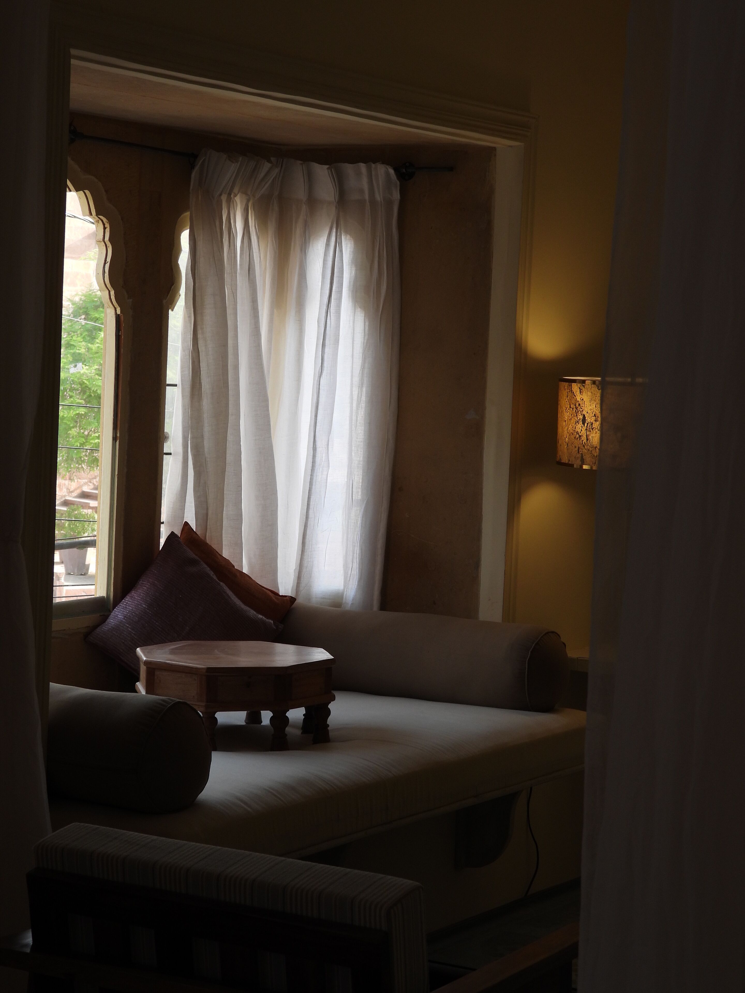 A cozy room with a cushioned bench, a small table, and a window with sheer curtains.