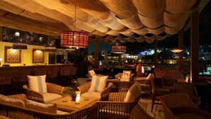 A cozy lounge area with wicker furniture, a pool table, and a bar with a view of the cityscape at night.