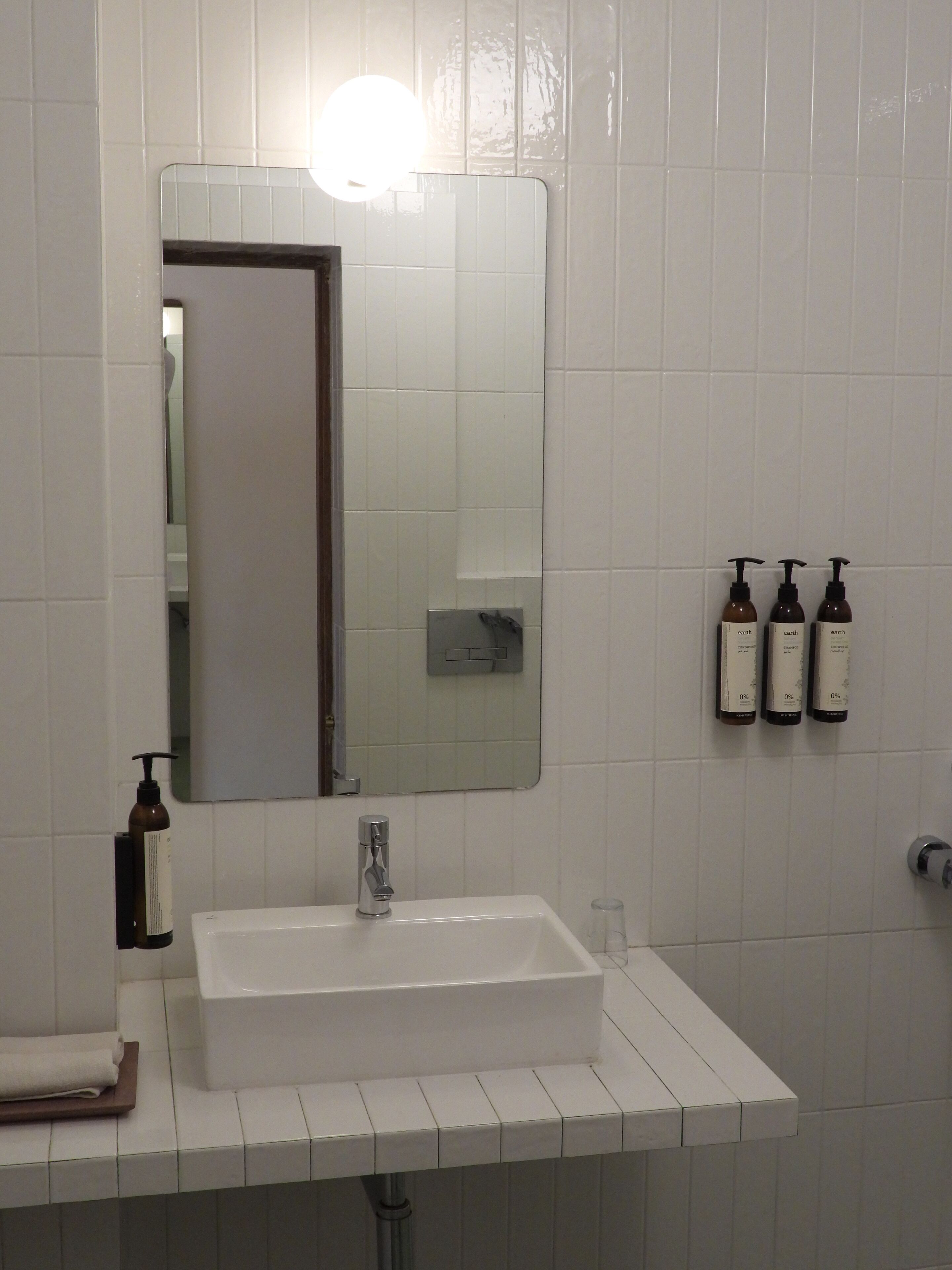 A bathroom with a white sink, a mirror, and three bottles of Earth brand shampoo.