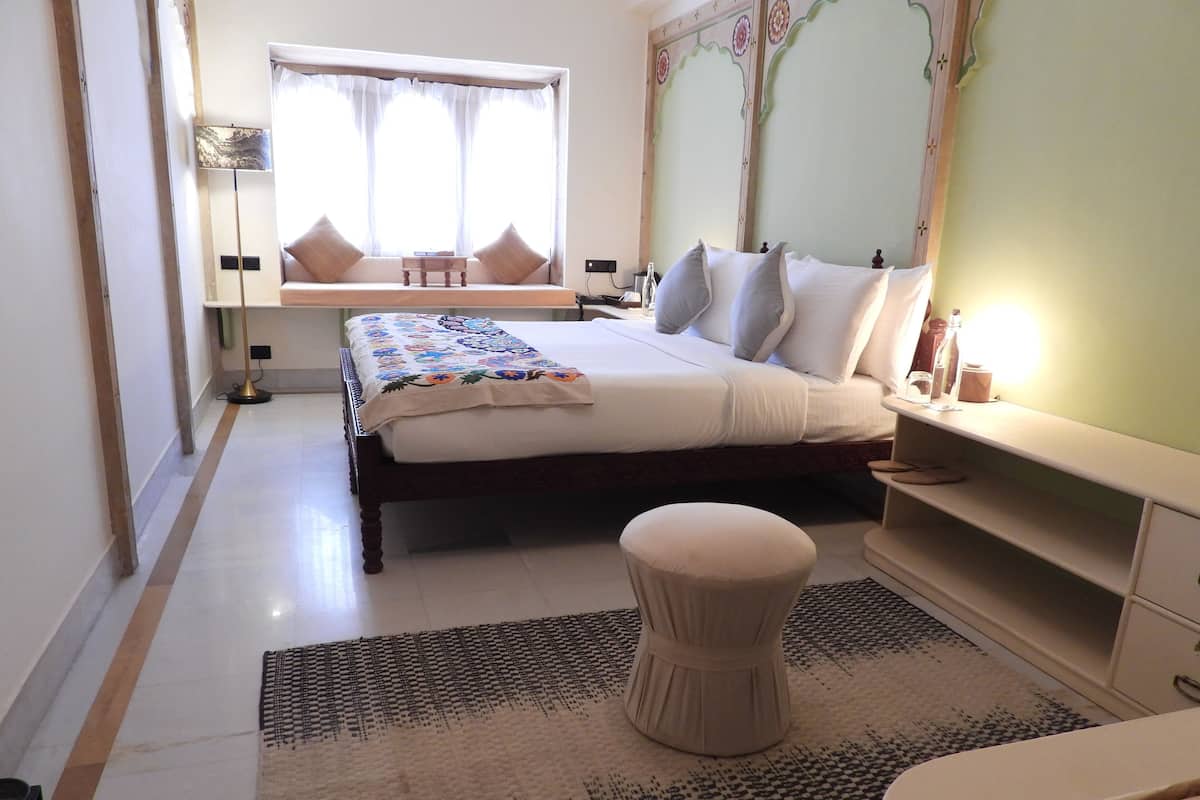 A bedroom with a bed, bedside tables, a nightstand, a window with curtains, a floor lamp, and a patterned rug.