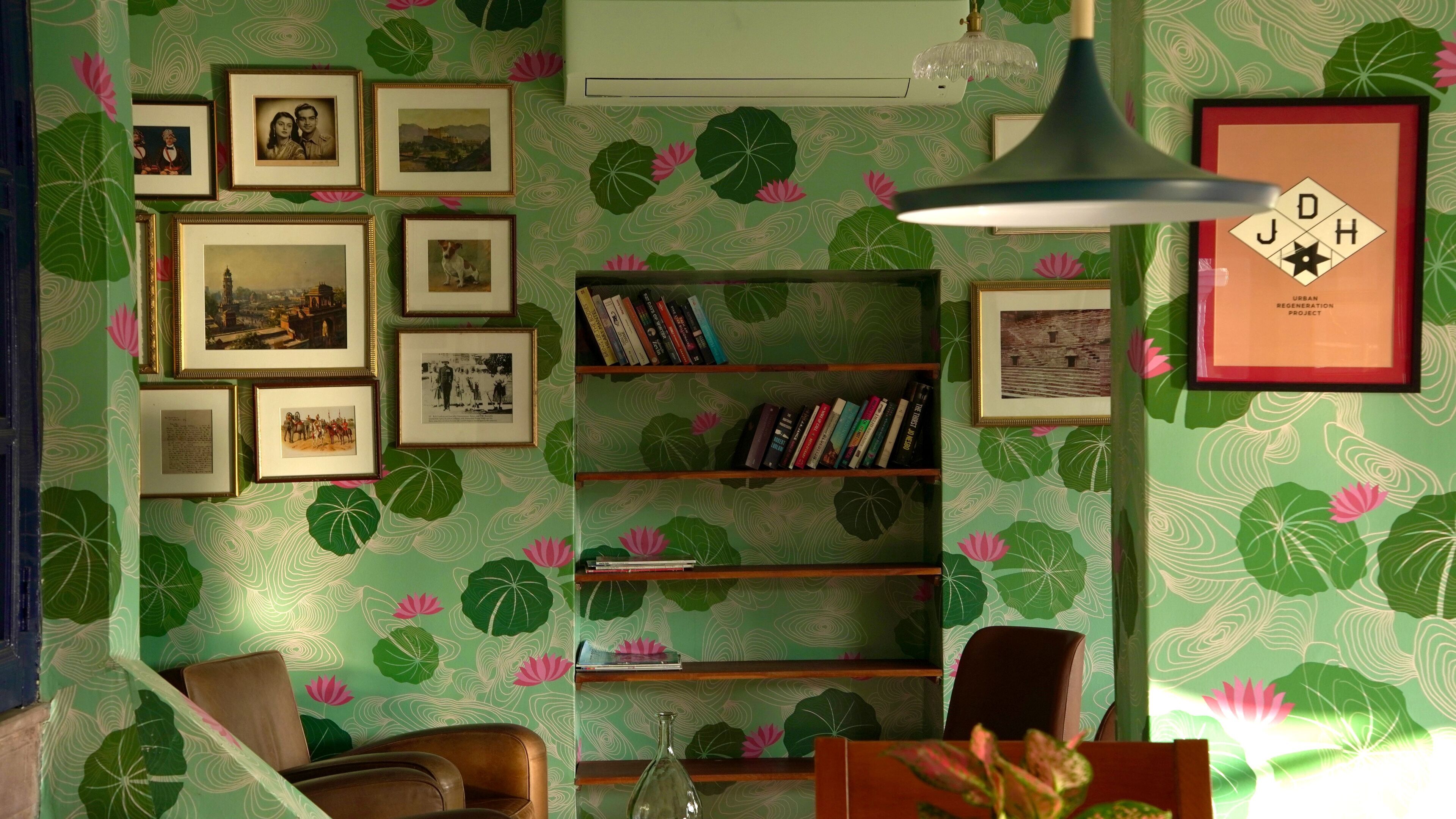 A room with a green patterned wallpaper, a bookshelf, framed pictures on the wall, and a brown leather chair.