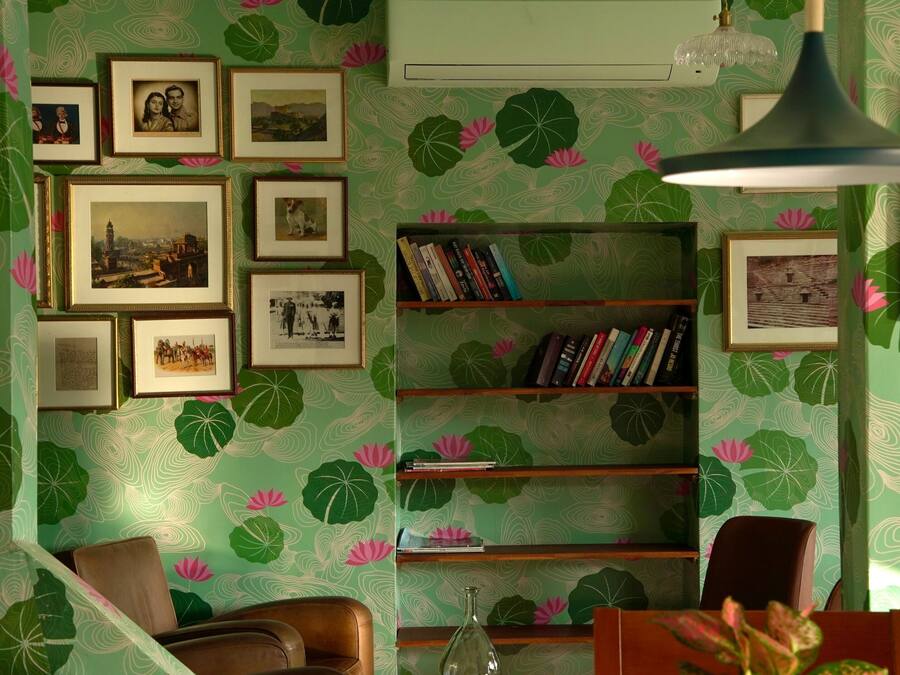 A room with a green patterned wallpaper, a bookshelf, framed pictures on the wall, and a brown leather chair.