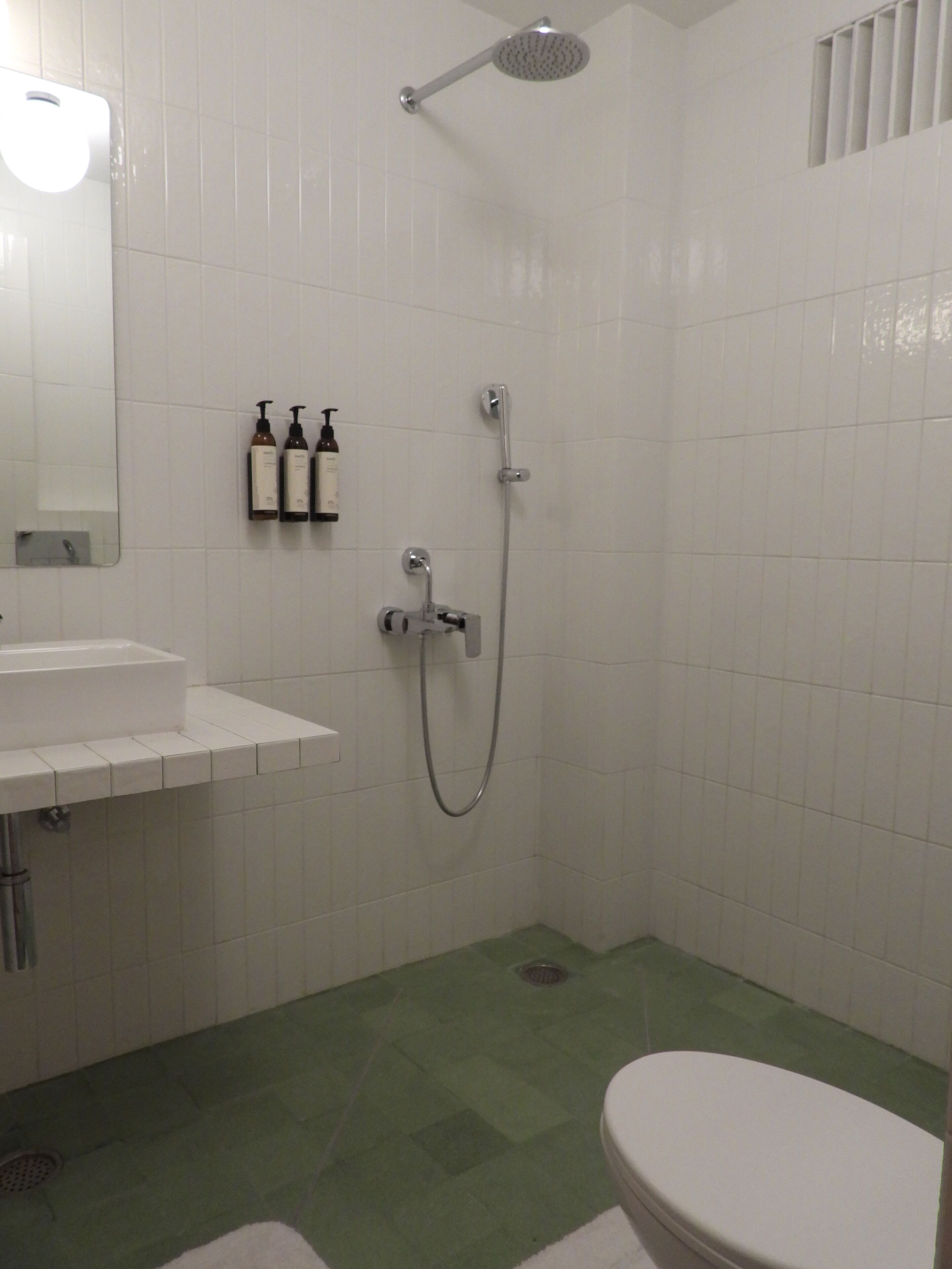 A bathroom with a shower, toilet, sink, and two bottles of shampoo on the wall.