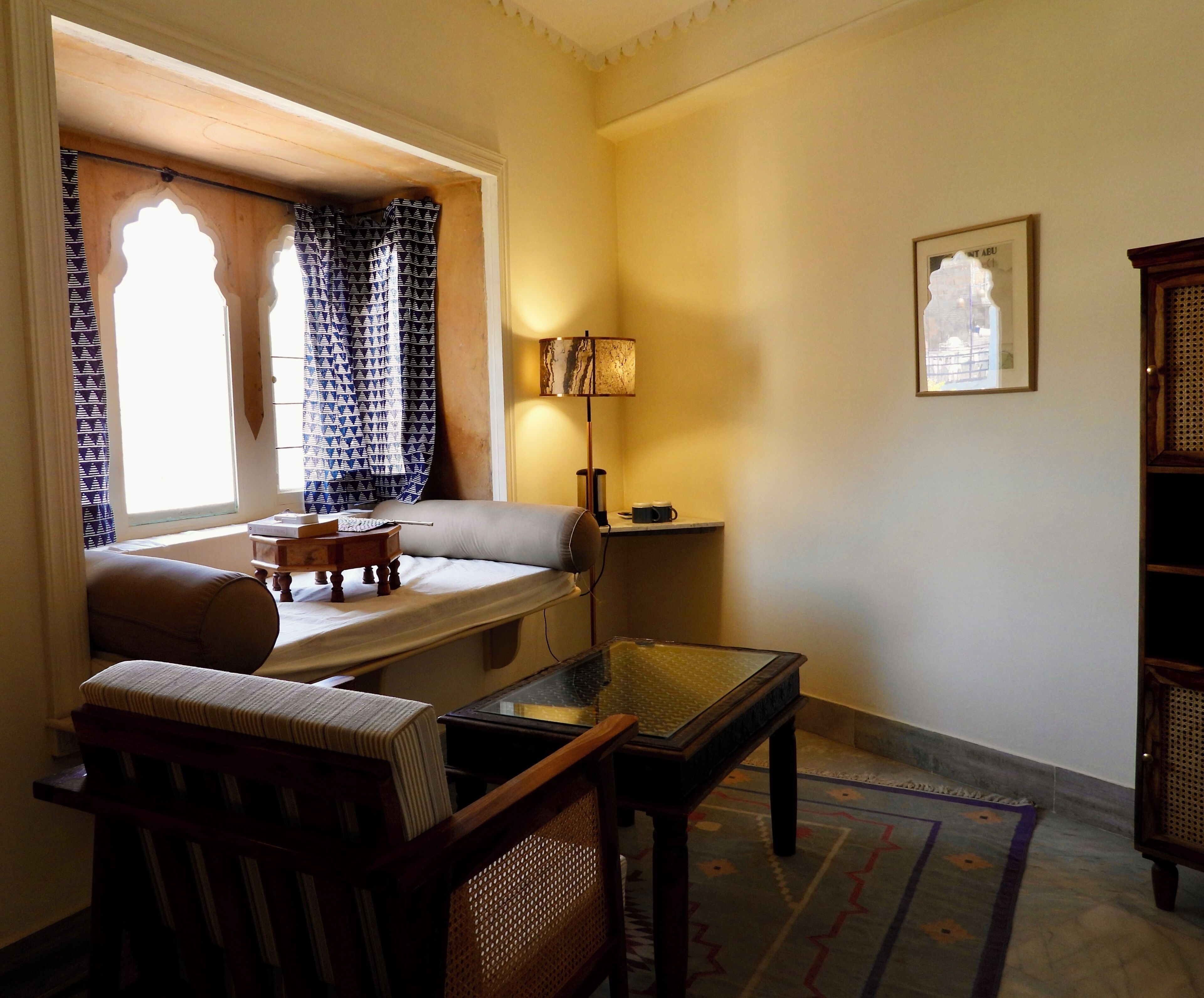 Una habitación acogedora con sofá, una mesita, lámpara y ventana con cortinas estampadas.