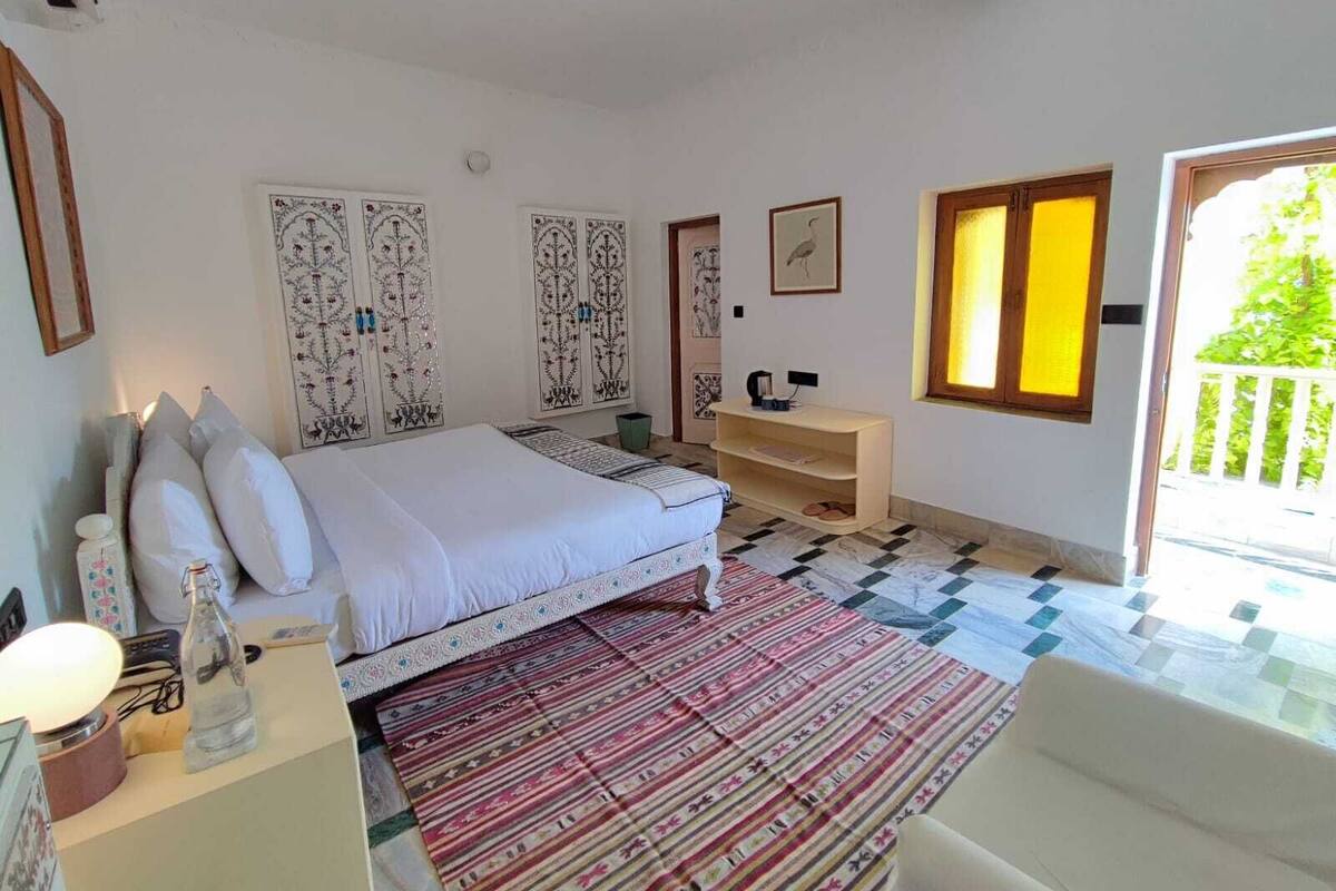 A bedroom with a bed, a bedside table, a chair, a window with a view, and a patterned rug.